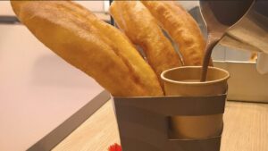 Kono de chocolate con churros sirviéndolo con la jarra de chocolate